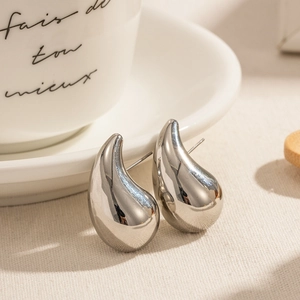Polished silver teardrop earrings on linen fabric with decorative ceramic cup background