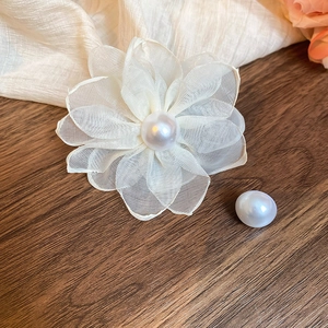Close-up of white chiffon flower earrings with pearls on dark wood and cream fabric