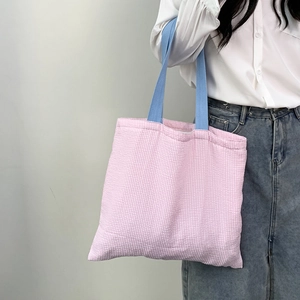 Detail of pink plaid canvas tote bag with contrast blue straps worn by a model