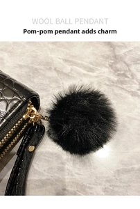 Close-up of a black faux fur ball pendant with gold chain on a crocodile pattern purse