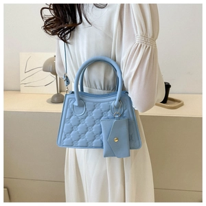 Detail of light blue quilted handbag and matching pouch held by model in bright room