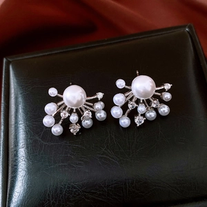 Close-up of pearl and zircon firework earrings on a premium textured leather surface