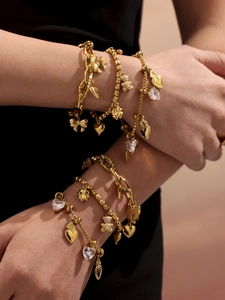 Close-up of stacked 18k gold plated bracelets with bear, heart, and clover charms
