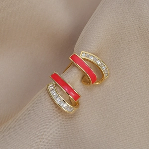 Detail view of gold earrings with red enamel and clear zircons on satin background