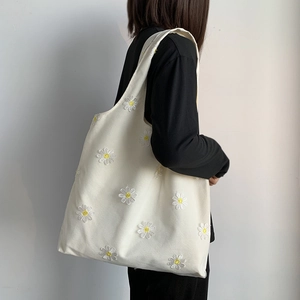 Close-up of a white canvas tote bag with detailed daisy embroidery and mesh texture