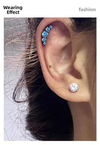 Detail view of blue five-gem curved barbell and stud earrings on ear cartilage