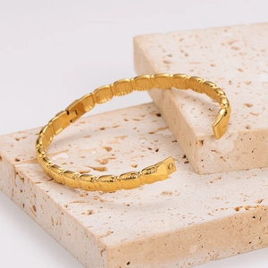 Elegant gold square textured stainless steel bangle bracelet on minimalist stone display