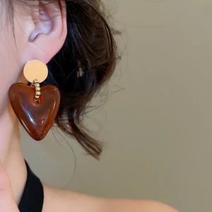 Close-up of a model wearing brown heart-shaped acrylic earrings with golden metal studs