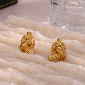 Macro shot of gold knotted earrings on white stone background with luxury metal texture