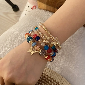 Detail of four bohemian beaded bracelets with gold butterfly charms on a model's wrist