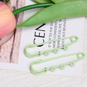 Close-up of light green lacquered metal safety pins with loops for DIY jewelry