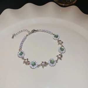 Detail of zircon flower bracelet with green stone and star charms on ceramic plate