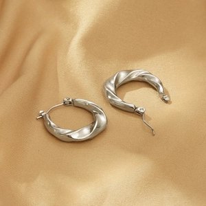 Detailed view of silver twisted C-shaped earrings on luxurious gold silk fabric