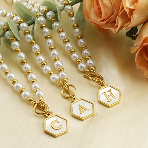 Collier doré à fermoir OT avec perle et pendentifs hexagonaux lettres A, C, H sur fond fleuri
