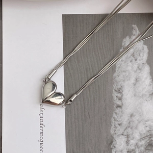 Macro detail of silver heart pendant with triple snake bone chains on card background
