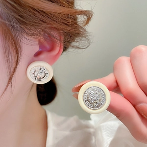 Détail de boucles d'oreilles carrées crème avec relief de pièce d'argent et bouton rétro