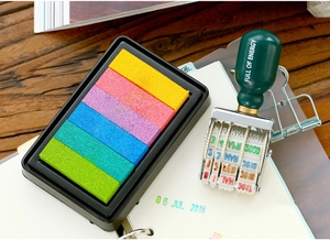 Close-up of a roller date stamp with 6-color gradient ink pad on a rustic wooden desk