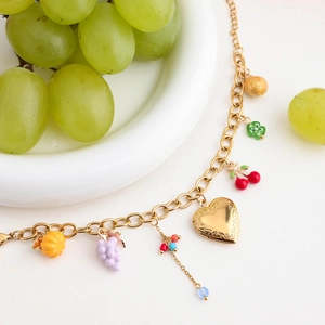 Detail of 18K gold-plated bracelet with heart lock and colorful fruit charms on ceramic