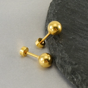 Detailed macro view of gold ball stud earrings featuring a secure screw-back closure design