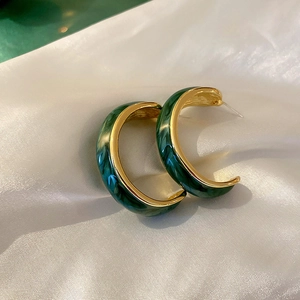 Detail of C-shaped emerald green marbled earrings with gold metal frame on silk fabric