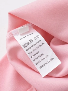 Detail of pink knitted fabric care label showing 100% polyester and washing instructions