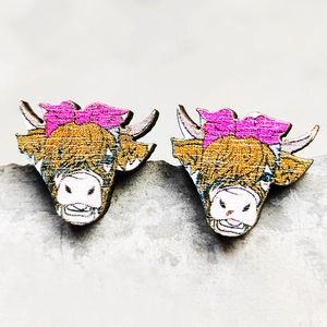Macro shot of wooden bull head stud earrings with a pink bow on a grey stone surface