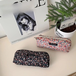 Close-up of floral corduroy pouches with metal zipper rings and brand label on desk