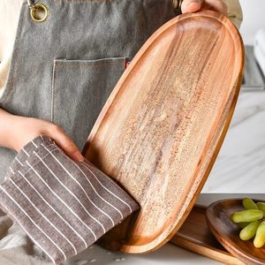 Oval wooden serving tray with natural grain being wiped by a striped cloth