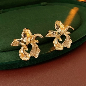 Macro shot of gold floral earrings with textured petals on green velvet display