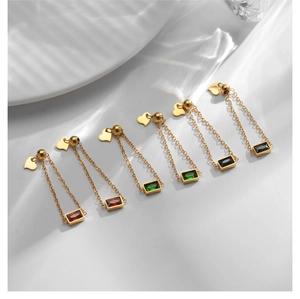 Close-up of heart-shaped gold earrings with long chains and colorful baguette gems