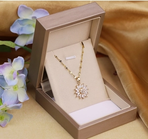 Detailed close-up of a gold daisy pendant necklace in a premium champagne jewelry box