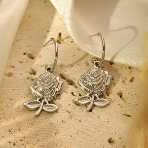 Macro shot of silver rose earrings with leaf stem on elegant silk background