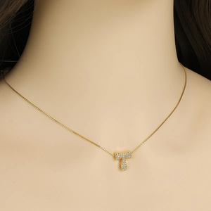 Close-up of a gold-toned necklace featuring a crystal-paved T letter pendant on a box chain