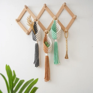 Three handmade bohemian macrame plant hangers in gray, red and green on a wooden rack
