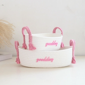 Detail of woven cotton storage baskets with pink tassels and goodday embroidery
