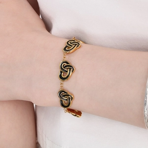 Detailed close-up of a gold heart-link bracelet with black enamel inlay on a woman's wrist