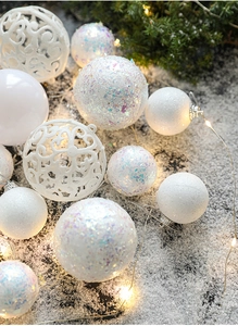 Close-up of assorted white Christmas ornaments on snow with warm festive lighting