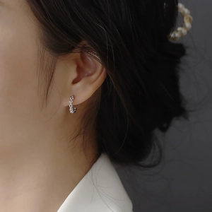 Close-up of a silver geometric watchband hoop earring with chain texture on a model