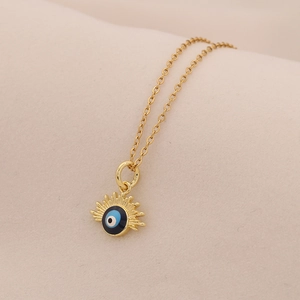 Dettaglio del ciondolo occhio dorato con smalto blu su sfondo in tessuto beige