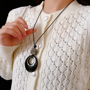Dettaglio della collana geometrica con pendente nero e perlina in pietra grigia su maglia