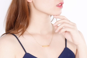 Detail of gold bar necklace with heart engraving and pink gemstone on a model's neck
