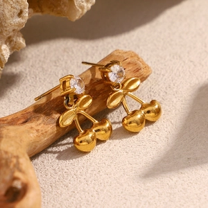Détail de boucles d'oreilles cerise plaquées or avec zircons sur un support en bois