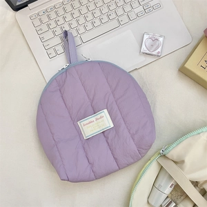 Detail of soft quilted purple makeup bag with a top handle and woven brand label