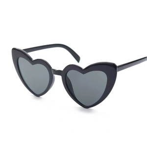 Detail view of heart-shaped sunglasses with black plastic frames and grey lenses