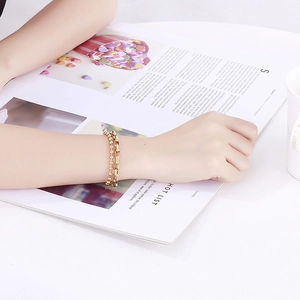 Detail view of a double-layered gold chain bracelet worn on a wrist over a magazine