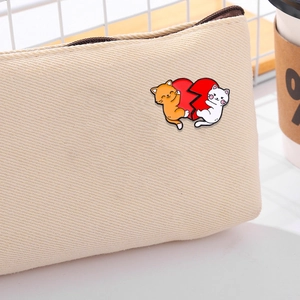 Detail of cartoon cat enamel pin with orange and white cats hugging a broken red heart