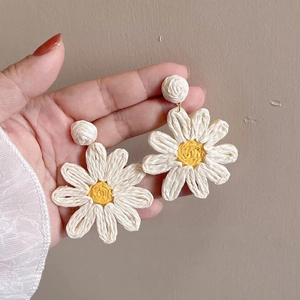 Detailed close-up of large woven daisy earrings with white petals and yellow centers