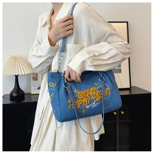Blue canvas tote bag with orange embroidery shown on a model in a casual setting