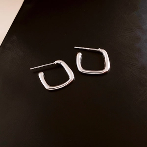 Close-up of geometric square silver leaf earrings on dark textured leather background