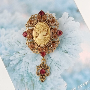 Dettaglio spilla cammeo vintage con cristalli rossi e decorazioni floreali dorate
